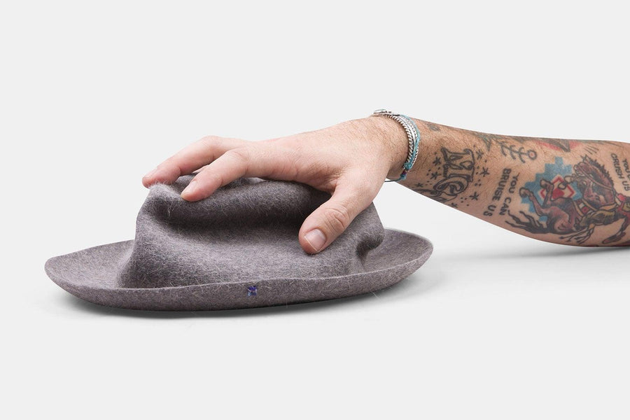 Hand touching a gray felt hat with a wide brim on a white background
