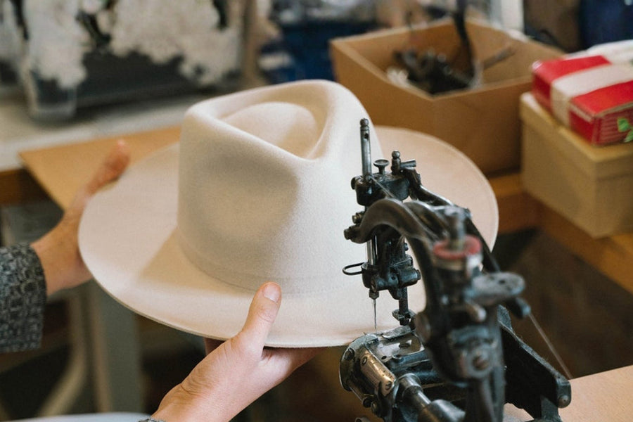 Hand shaping a cream felt hat on a sewing machine in a workshop