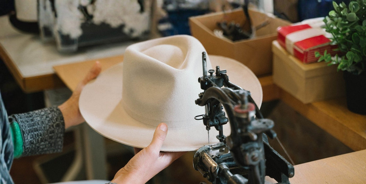 Hand shaping a cream felt hat on a sewing machine in a workshop