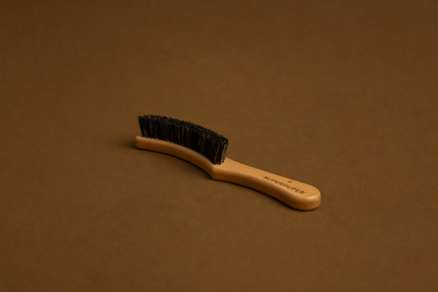 Curved wooden hat brush with black bristles on brown background for hat cleaning