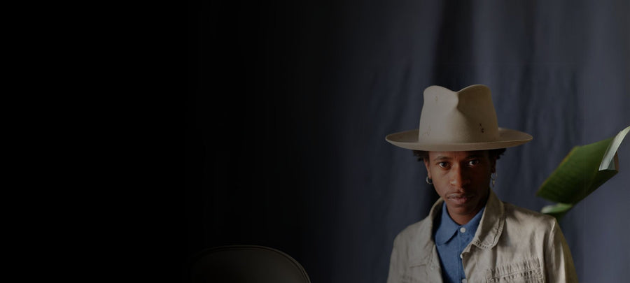 Man wearing a handmade felt hat and light jacket in a studio with a dark backdrop