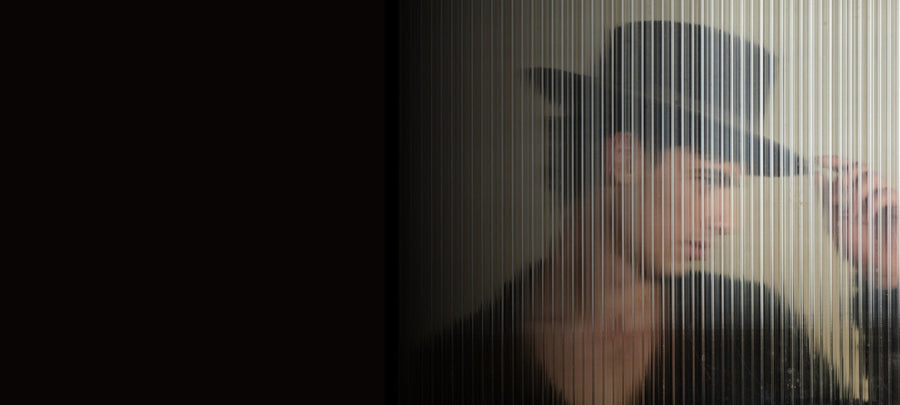 Person in a black felt hat behind frosted glass, artistic hat fashion photo