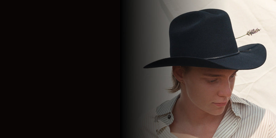 Young man wearing handmade black felt wide-brim hat with lavender stem, striped shirt