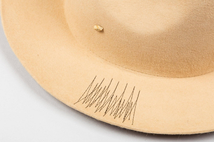 Beige felt hat with black stitched detail on brim and small decorative accent