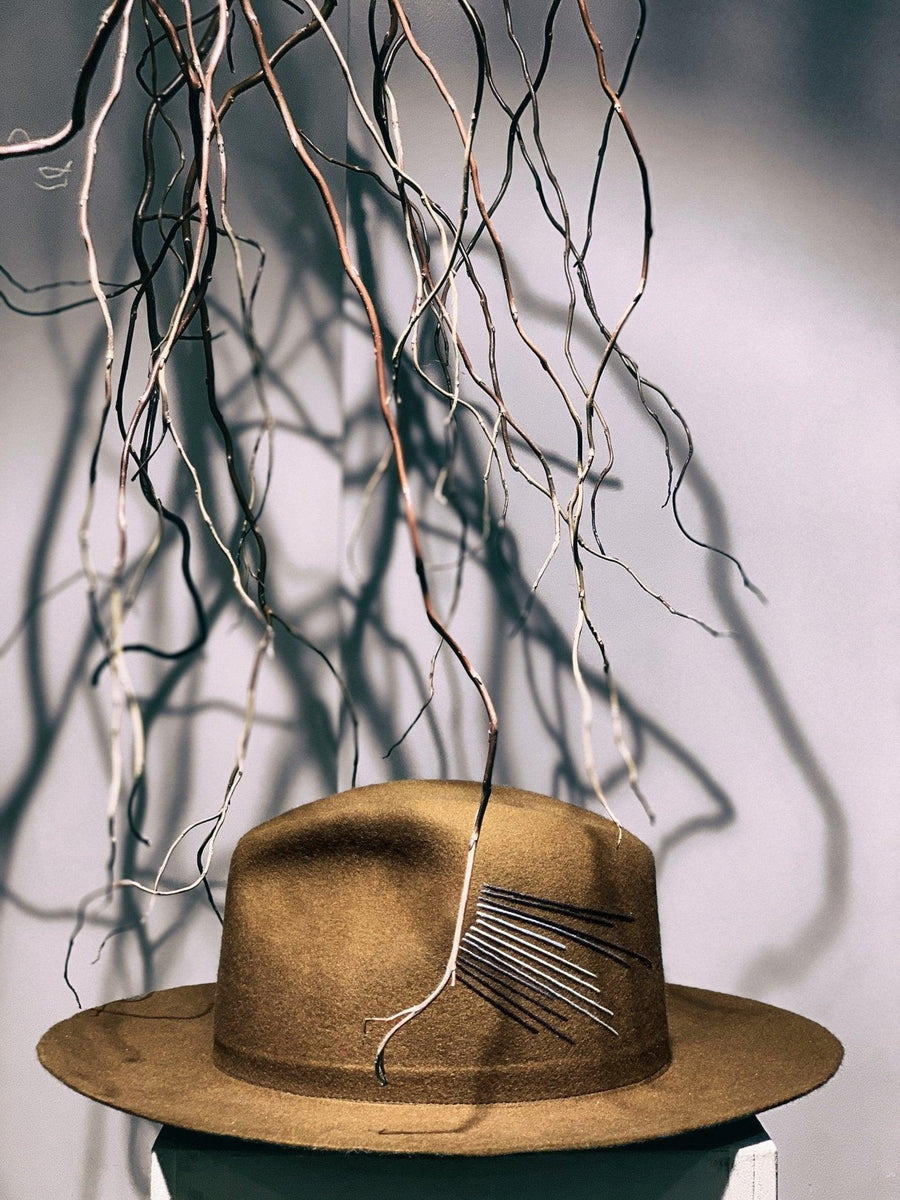 Brown premium felt wide-brim hat with stitched detail, displayed with hanging twigs.