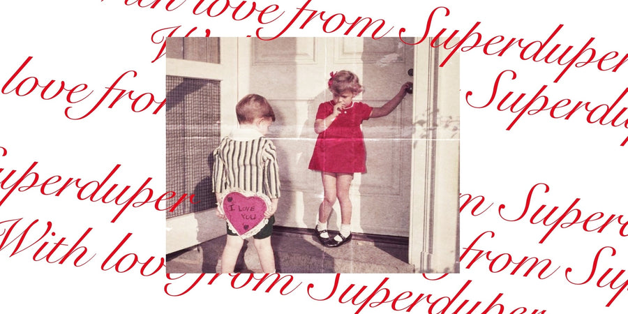 Vintage style photo of a boy with a heart-shaped sign reading 'I love you' and a girl in red.