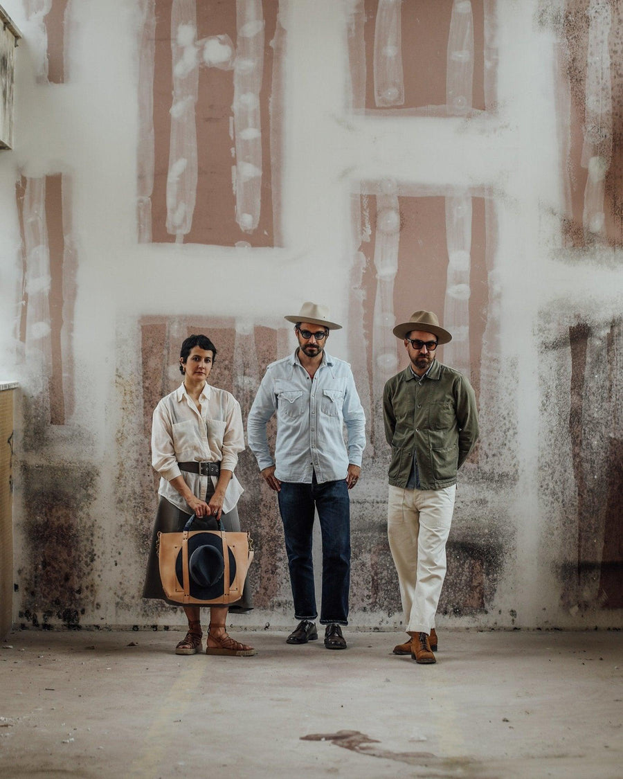 Three people wearing stylish Italian hats and casual clothing in an industrial setting